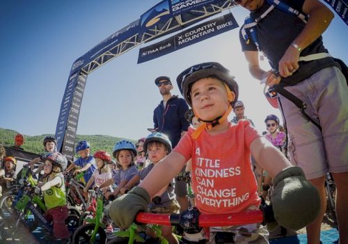 Children with helmets on their bikes at a starting line for a race, one in a red shirt that reads 