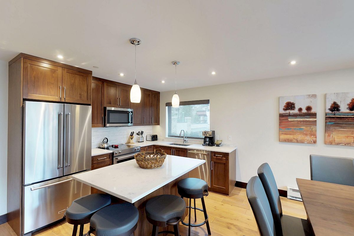 Modern kitchen featuring wood cabinets, stainless steel appliances, an island with stools, pendant lighting, a window, and artwork on the wall.