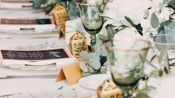 A beautifully decorated table set for an event, featuring green goblets, white flowers, intricate gold lanterns, and menus placed at each setting.