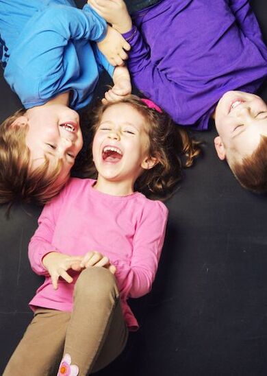 Three children are lying on the ground, laughing and enjoying each other's company. They appear to be having a joyous time together.