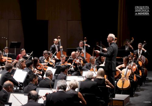 A conductor leads an orchestra during a performance; musicians play various instruments, with 