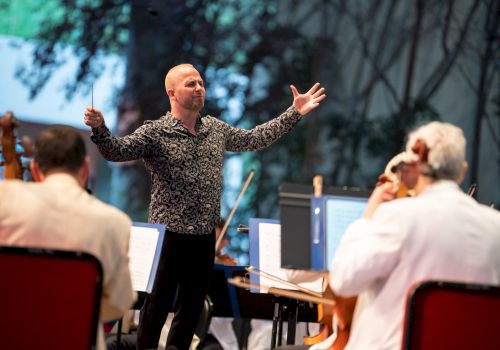 A conductor enthusiastically leads an orchestra during a performance, with musicians attentively playing their instruments and following his directions.