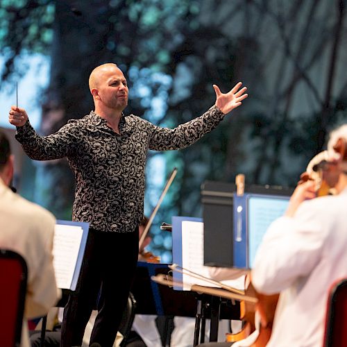 A conductor enthusiastically leads an orchestra during a performance, with musicians attentively playing their instruments and following his directions.